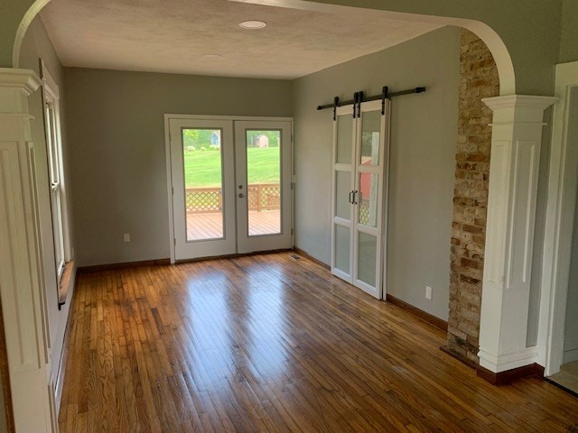 interior space featuring french doors, a barn door, dark hardwood / wood-style floors, and decorative columns