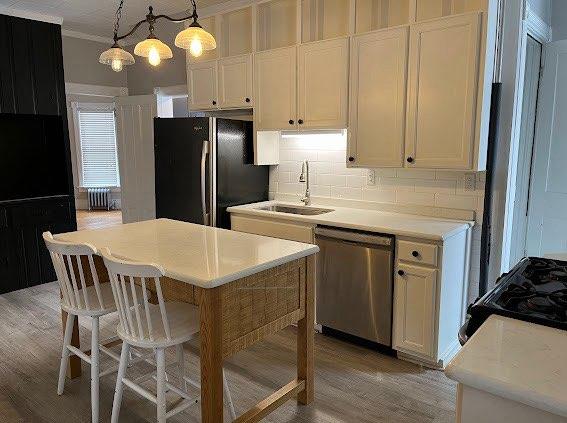 kitchen featuring radiator, dishwasher, sink, pendant lighting, and white cabinets