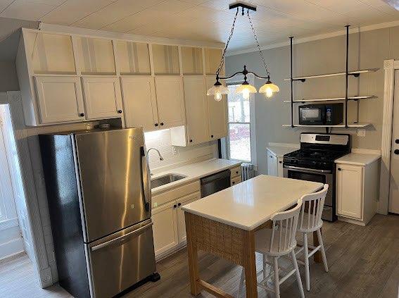 kitchen with dark wood-type flooring, white cabinets, sink, hanging light fixtures, and stainless steel appliances