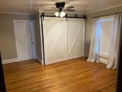 unfurnished bedroom with a barn door, light hardwood / wood-style flooring, and ceiling fan