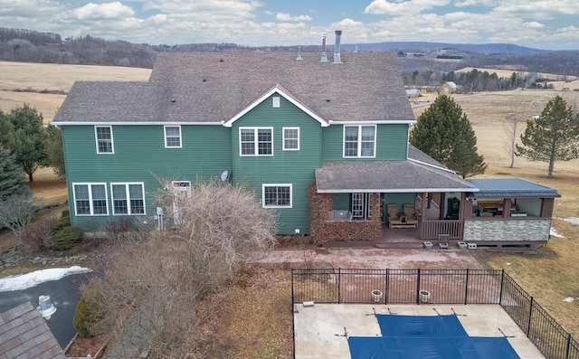 rear view of property featuring a shingled roof and fence