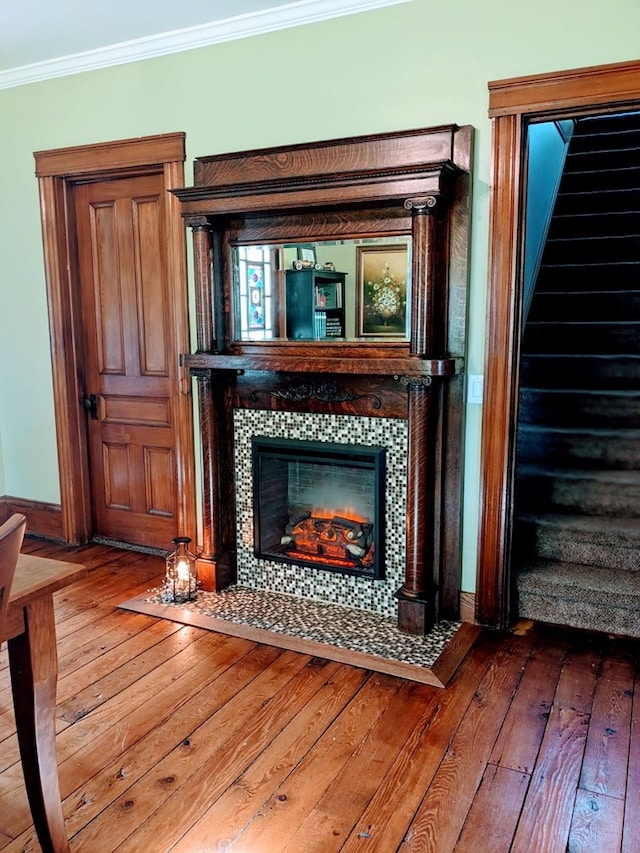 interior space with wood-type flooring, ornamental molding, and a tiled fireplace