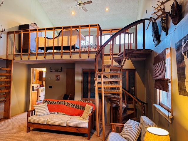 living room with ceiling fan, a towering ceiling, a textured ceiling, and carpet