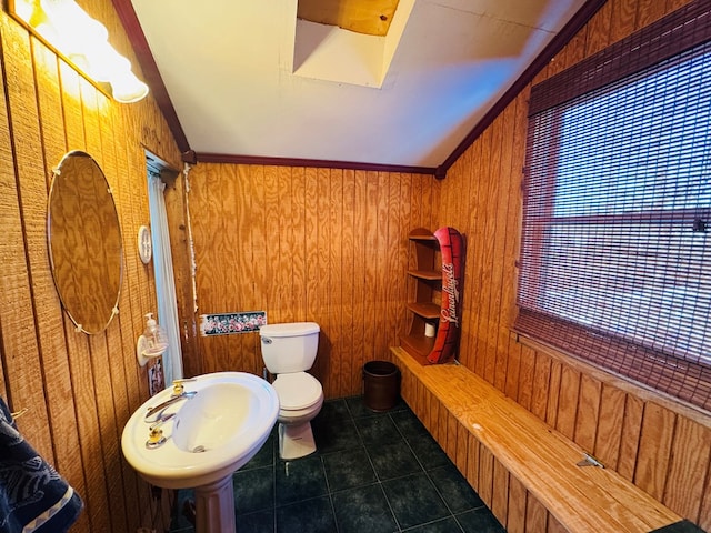 bathroom with lofted ceiling with skylight, sink, and wood walls