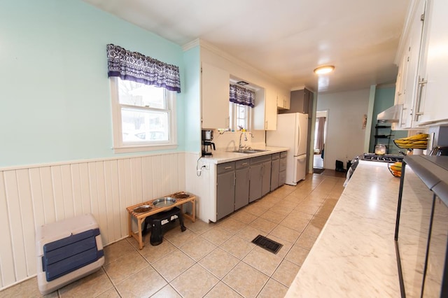 kitchen featuring gas range, sink, light tile patterned floors, white cabinets, and white fridge