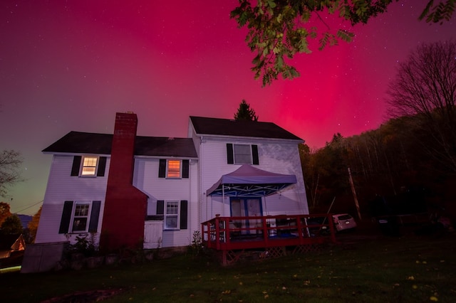 back house at dusk with a gazebo, a wooden deck, and a lawn