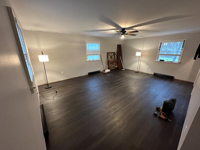 unfurnished living room with a wealth of natural light, ceiling fan, dark hardwood / wood-style floors, and a baseboard heating unit