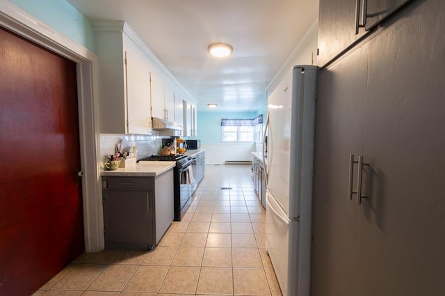 kitchen with decorative backsplash, gas range, light tile patterned floors, white cabinets, and white fridge