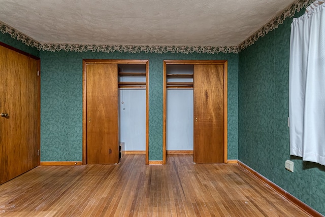 unfurnished bedroom with hardwood / wood-style flooring, a textured ceiling, and multiple closets