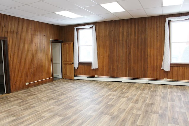 spare room featuring a baseboard heating unit, wood walls, light hardwood / wood-style floors, and a drop ceiling