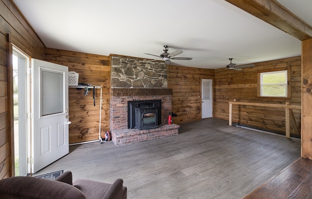 unfurnished living room featuring wood walls, a wood stove, dark hardwood / wood-style floors, ceiling fan, and beamed ceiling