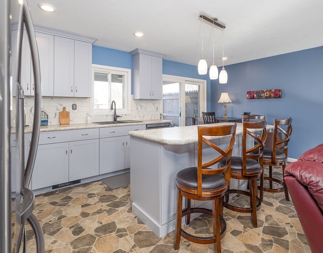 kitchen featuring a center island, tasteful backsplash, stainless steel refrigerator, sink, and decorative light fixtures