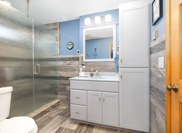 bathroom with a shower with door, toilet, vanity, and tile walls