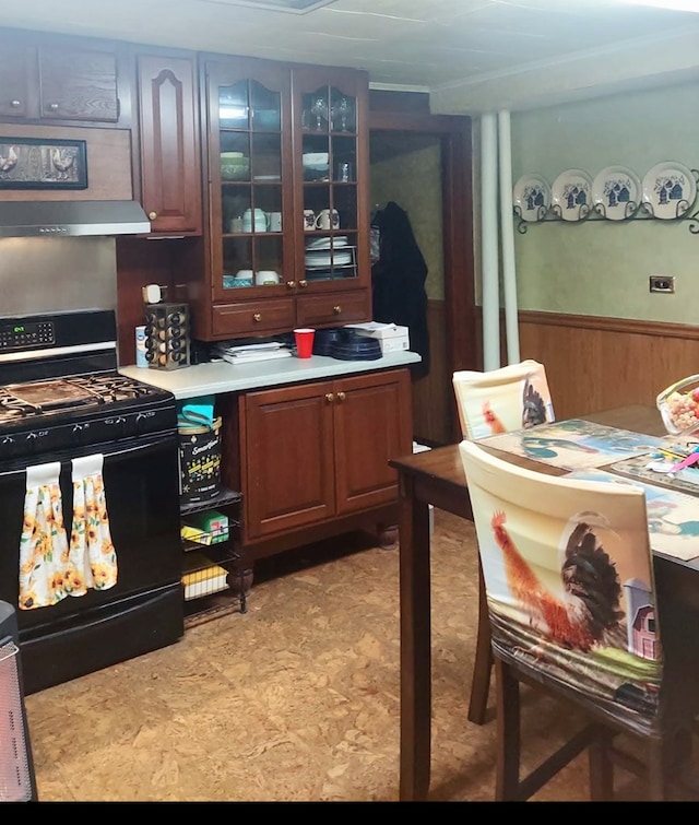 kitchen with wainscoting, glass insert cabinets, range hood, light countertops, and black gas stove