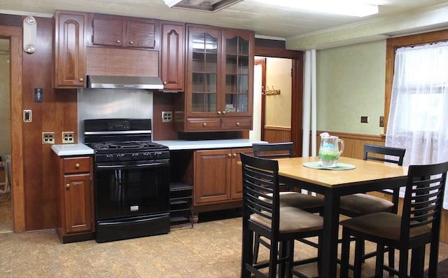 kitchen with range hood, a wainscoted wall, light countertops, glass insert cabinets, and gas stove