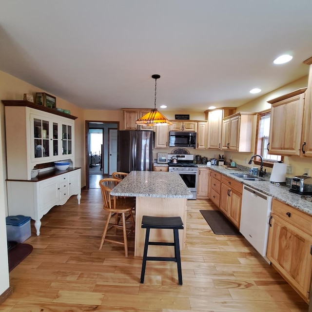 kitchen with light brown cabinets, stainless steel appliances, a kitchen island, a sink, and light wood finished floors