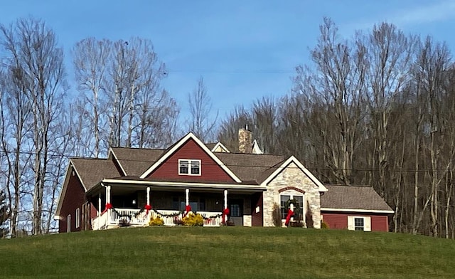 view of front of home featuring a porch, a front yard, stone siding, and a chimney