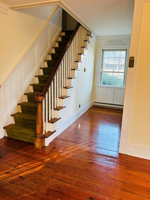 stairs with baseboard heating, wood-type flooring, and ornamental molding