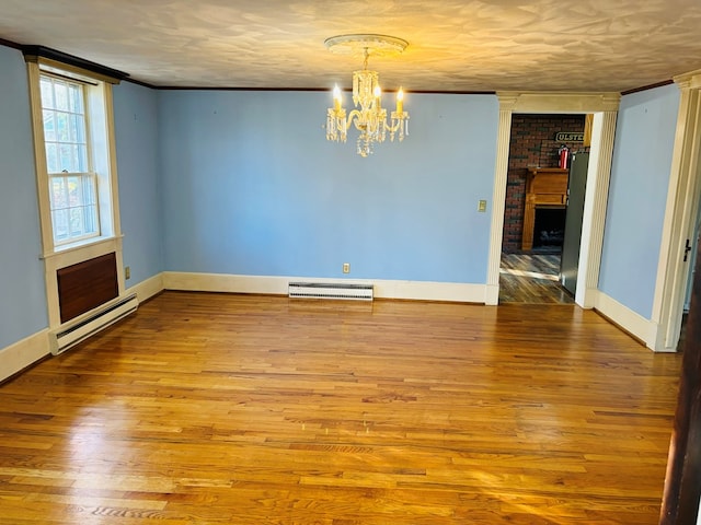 empty room with crown molding, a chandelier, light hardwood / wood-style floors, and baseboard heating