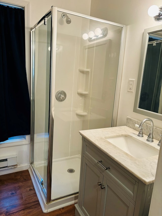 bathroom featuring a baseboard heating unit, hardwood / wood-style flooring, an enclosed shower, and vanity