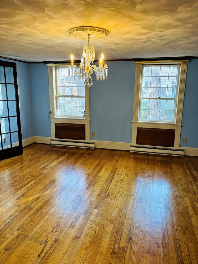 spare room featuring baseboard heating, wood-type flooring, a chandelier, and a textured ceiling