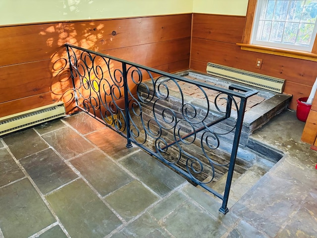 stairway featuring a baseboard heating unit and wooden walls