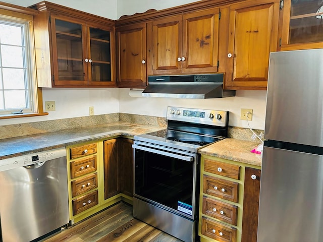 kitchen with appliances with stainless steel finishes, dark hardwood / wood-style flooring, and light stone counters