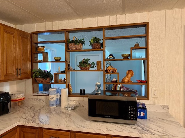 interior details featuring brown cabinets, open shelves, light countertops, a textured ceiling, and stainless steel microwave