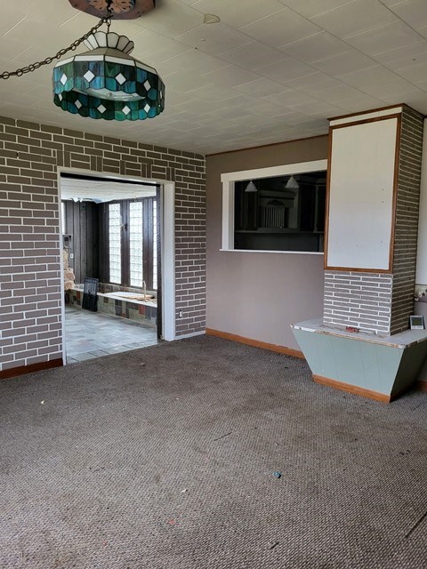 unfurnished living room featuring carpet and brick wall