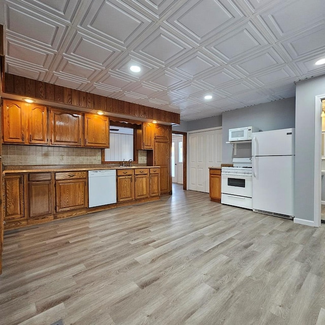 kitchen with tasteful backsplash, white appliances, and light hardwood / wood-style floors