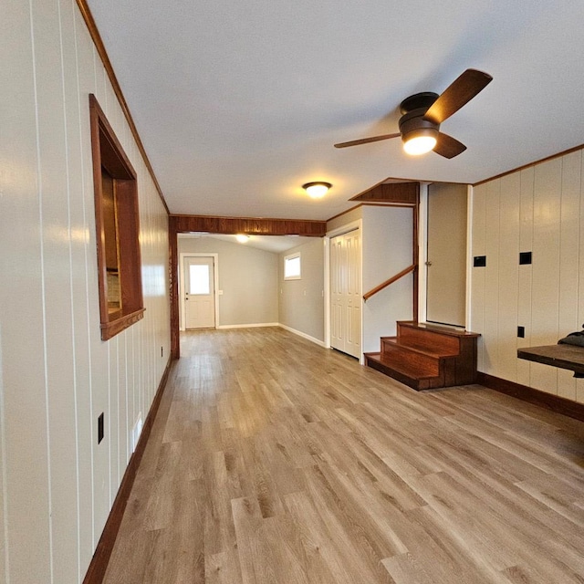 interior space with ornamental molding, wood walls, ceiling fan, and light hardwood / wood-style flooring