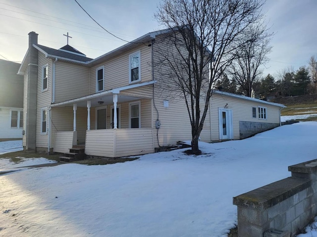 snow covered back of property featuring a porch