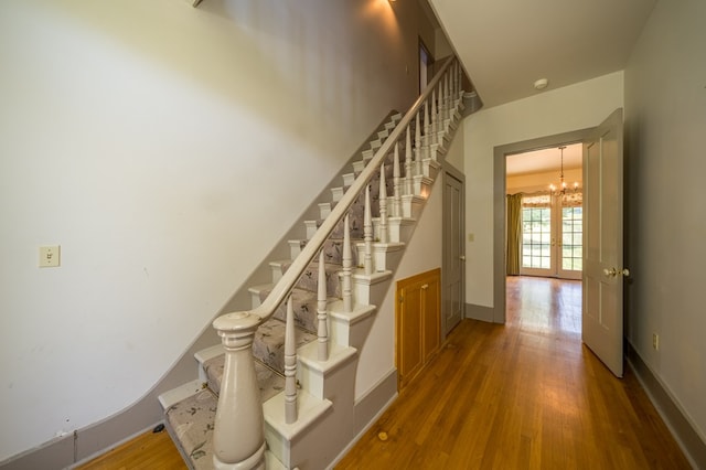 staircase featuring hardwood / wood-style floors, an inviting chandelier, and french doors