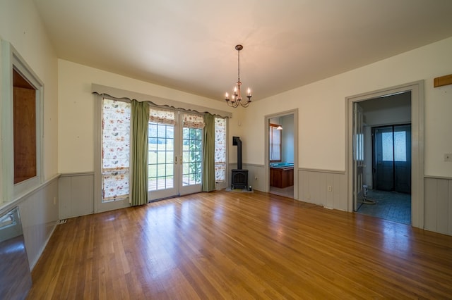 unfurnished room featuring hardwood / wood-style floors, a notable chandelier, and a wood stove