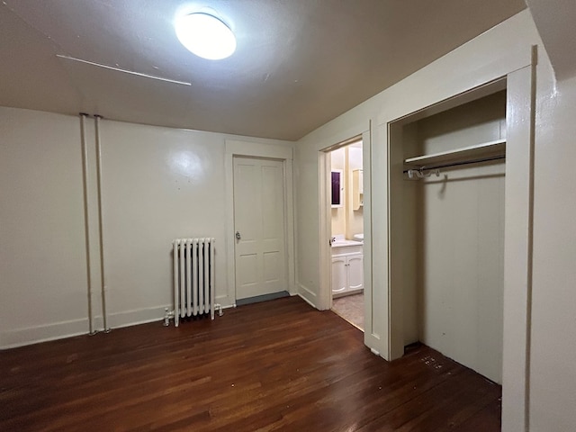 unfurnished bedroom with radiator, a closet, ensuite bath, and dark hardwood / wood-style floors