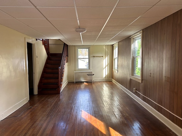 unfurnished room featuring radiator, wood walls, plenty of natural light, and dark hardwood / wood-style floors