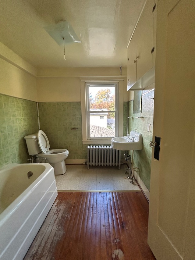 bathroom featuring a washtub, toilet, radiator heating unit, and wood-type flooring