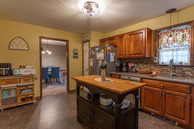 kitchen featuring pendant lighting, sink, tasteful backsplash, dishwashing machine, and stainless steel refrigerator