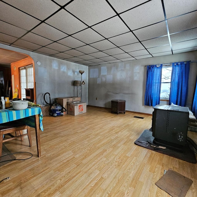 rec room with a wood stove, a paneled ceiling, and hardwood / wood-style flooring