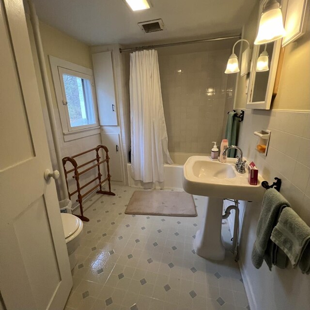 bathroom with shower / bathtub combination with curtain, tile walls, and toilet