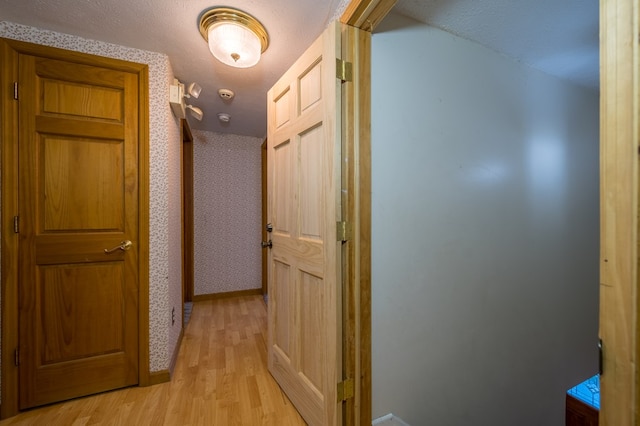 corridor featuring light wood-type flooring and a textured ceiling