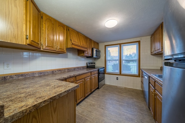 kitchen featuring sink, a textured ceiling, tasteful backsplash, wood-type flooring, and stainless steel appliances