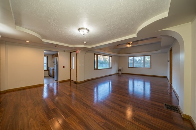 empty room with dark hardwood / wood-style floors, ceiling fan, a raised ceiling, and a textured ceiling