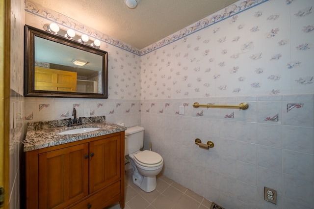 bathroom with tile patterned flooring, a textured ceiling, toilet, vanity, and tile walls