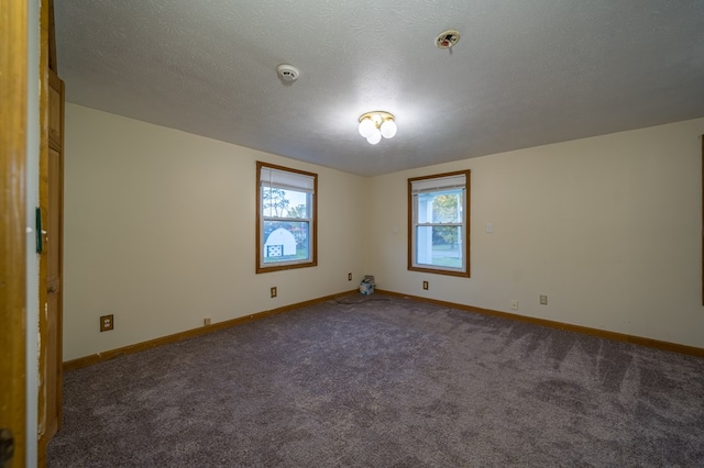 spare room with a textured ceiling and dark colored carpet