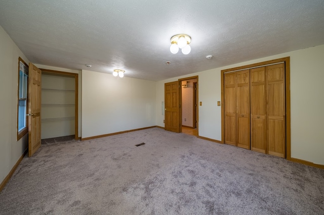 unfurnished bedroom with light colored carpet, a textured ceiling, and multiple closets