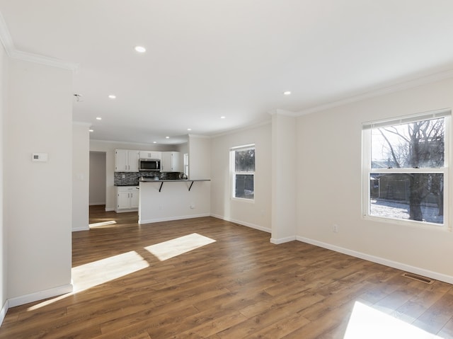 unfurnished living room featuring dark hardwood / wood-style flooring, ornamental molding, and a wealth of natural light