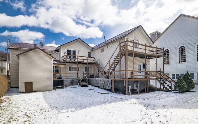 snow covered rear of property featuring stairway, metal roof, and a wooden deck