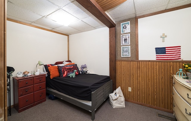 bedroom featuring a paneled ceiling, wainscoting, wood walls, and carpet