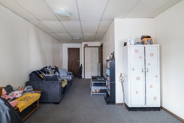 living room with baseboards, dark carpet, and a drop ceiling